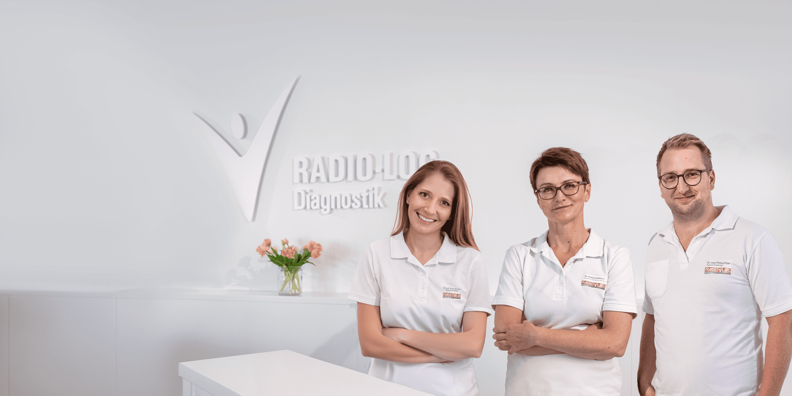 Drei Mitarbeiterinnen im weißen Kittel am Empfang des Mammographie Screening Niederbayern, mit Blumen und Diagnostik-Schild.