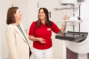 Zwei Frauen an einem Mammographiegerät im Screening-Zentrum: Eine Fachkraft erklärt einer Patientin den Ablauf der Brustkrebsfrüherkennung.